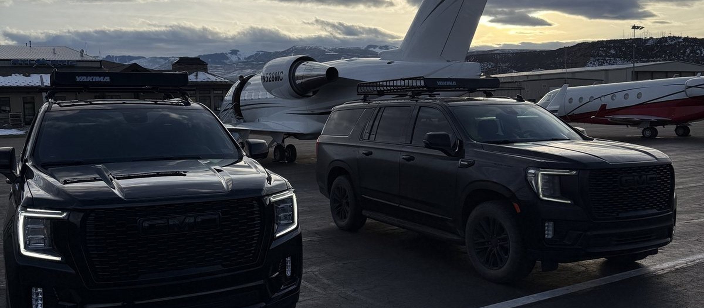 Two black GMC SUVs beside a private jet on the tarmac at Aspen/Pitkin County Airport