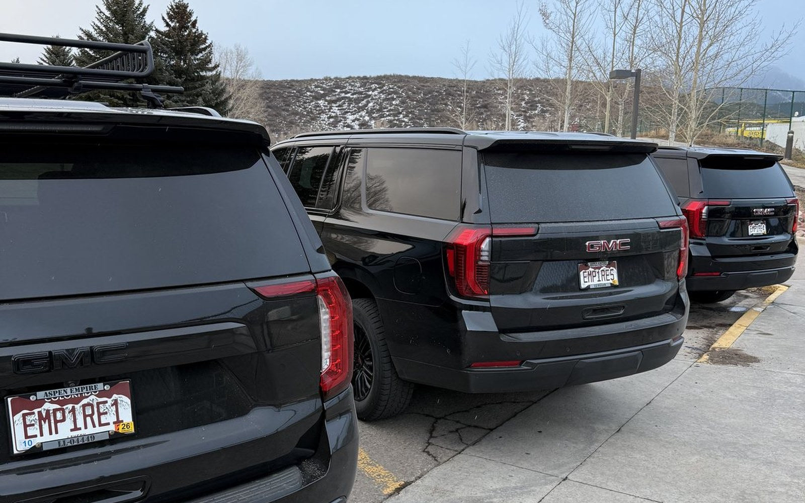 Three black GMC Yukons lined up with Aspen Empire EMP1RE plates, mountains behind