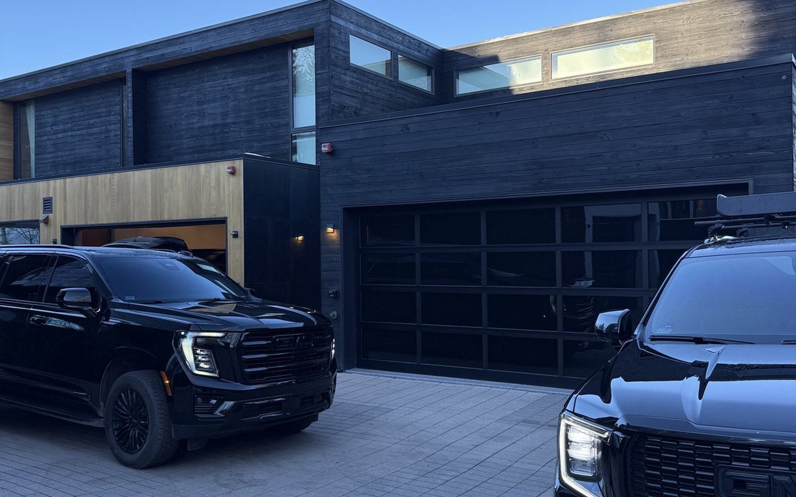 Two black GMC SUVs waiting on the driveway of a modern timber-clad Aspen residence