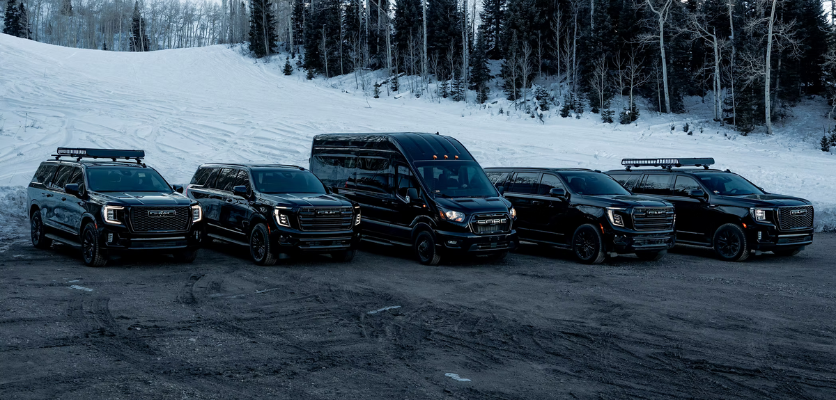 Aspen Empire's five-vehicle fleet of black SUVs and a Ford Transit van lined up on a snowy road at dusk