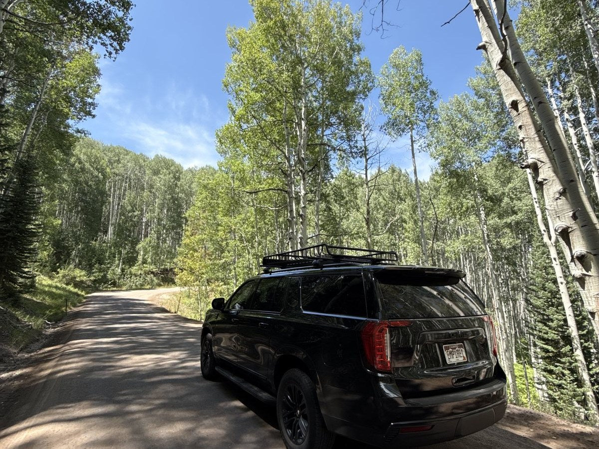Black GMC Yukon on a dirt road through summer aspen forest outside Aspen