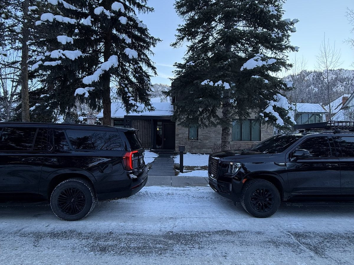 Two black GMC SUVs waiting outside a modern Aspen residence in fresh snow