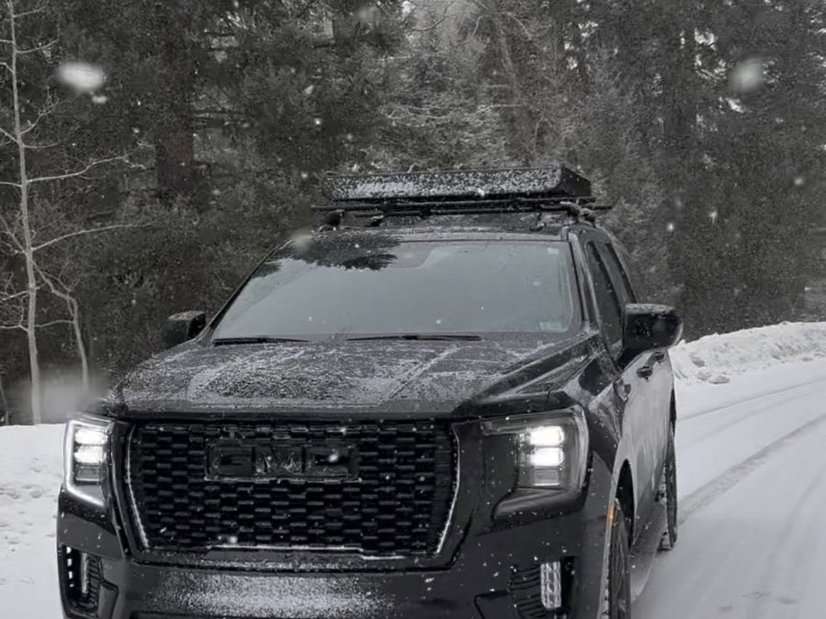 Black GMC Yukon XL driving a snow-covered forest road in falling snow near Aspen